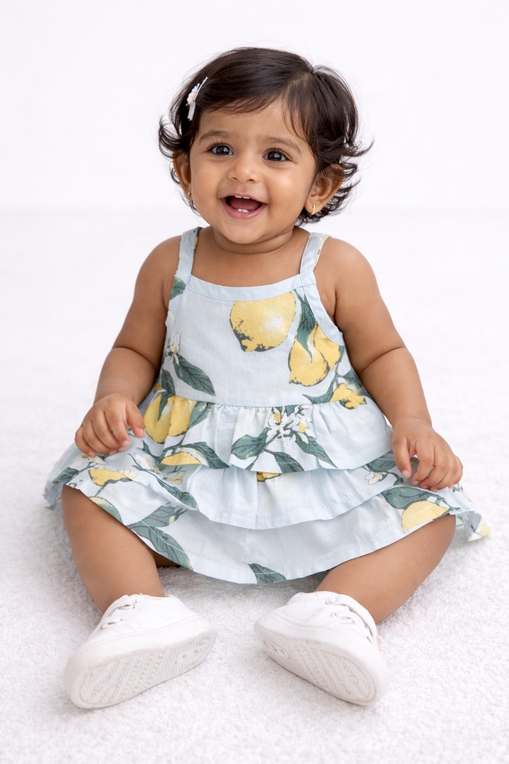 Baby girl sitting in a lemon print tiered cotton frock while seated