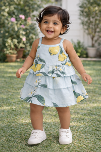 Baby girl wearing a lemon print tiered cotton frock outdoors