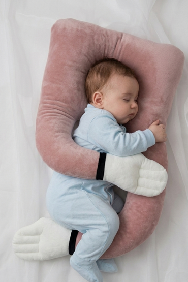 Baby resting on a blush pink U-shaped Baby Hug Pillow with padded side cushions